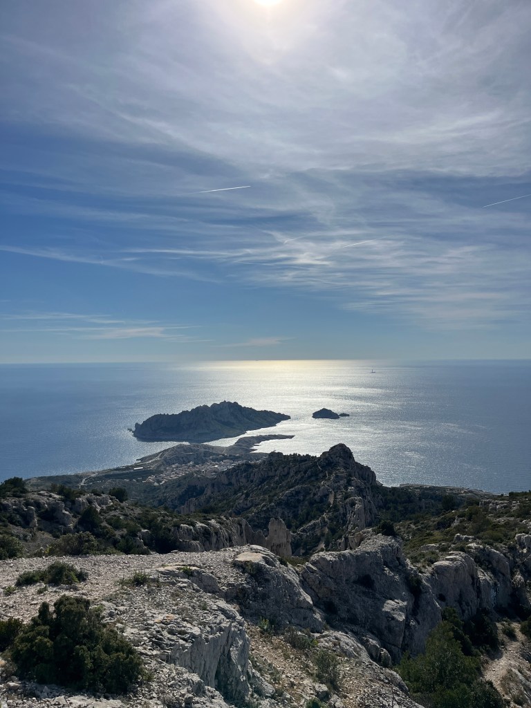 View from a rocky ridge over the sea, with the sun on the water and a small island off the coast